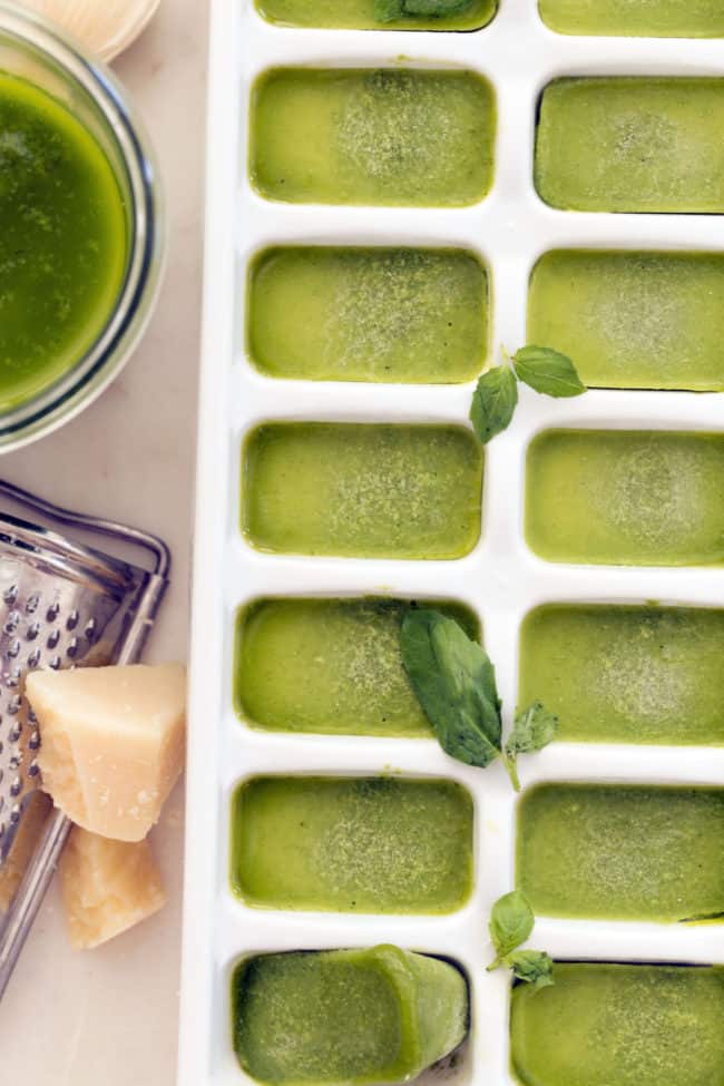 A white ice cube tray filled with frozen pesto cubes