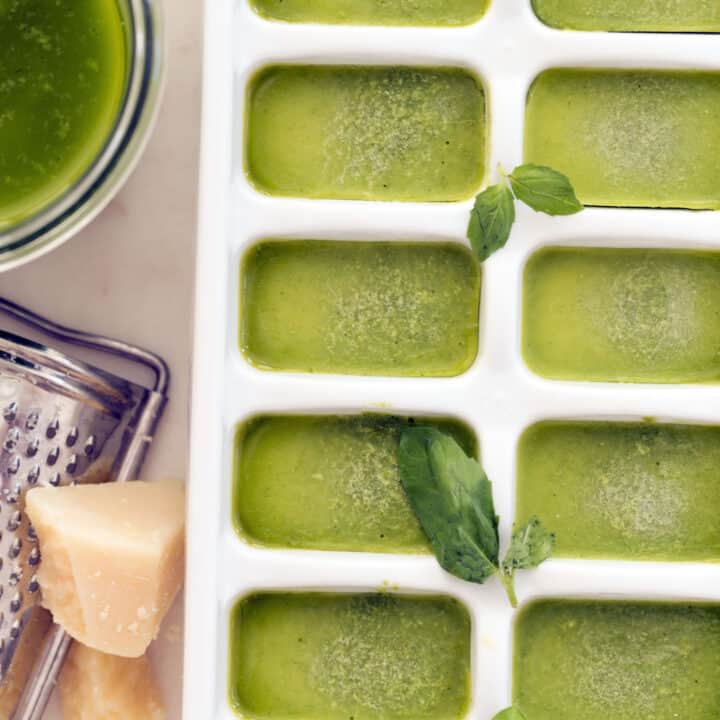 A white ice cube tray filled with frozen pesto cubes.