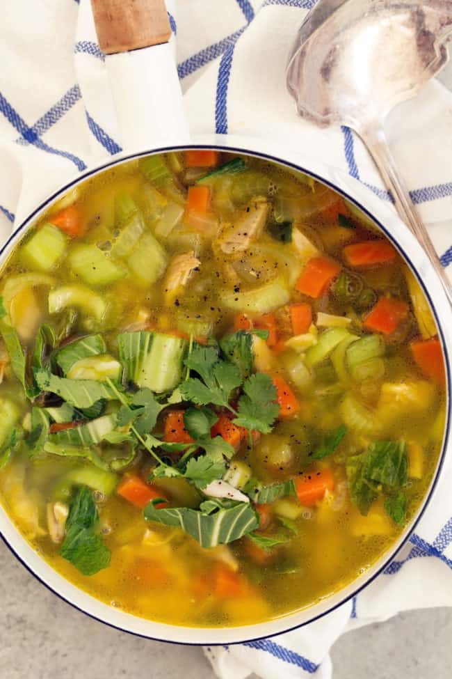 A white pot filled with chicken vegetable soup.