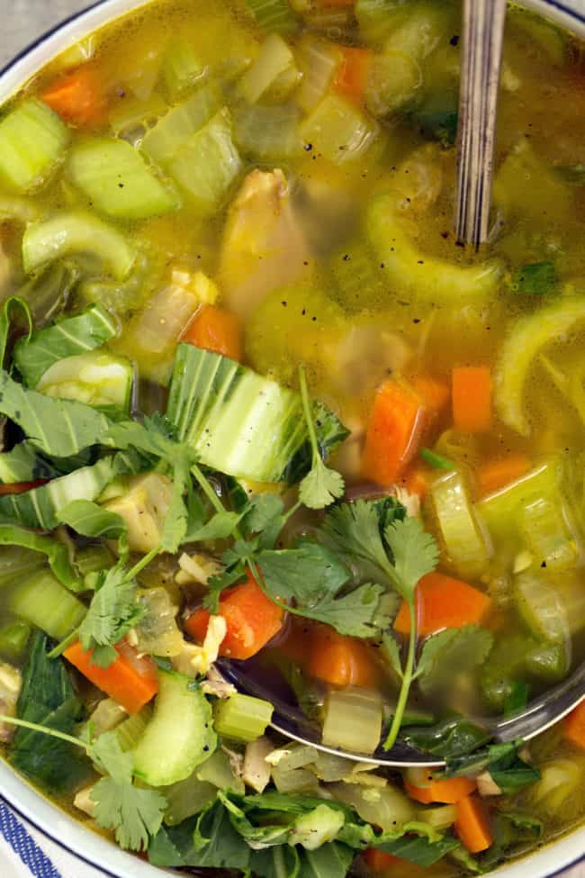 A white pot filled with immune boosting chicken soup. A silver ladle rests in the pot.