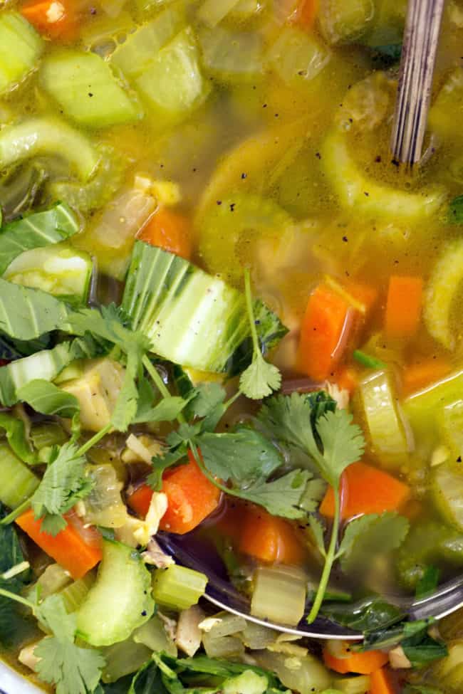 A white pot filled with vegetables and broth. A silver ladle rests in the pot.