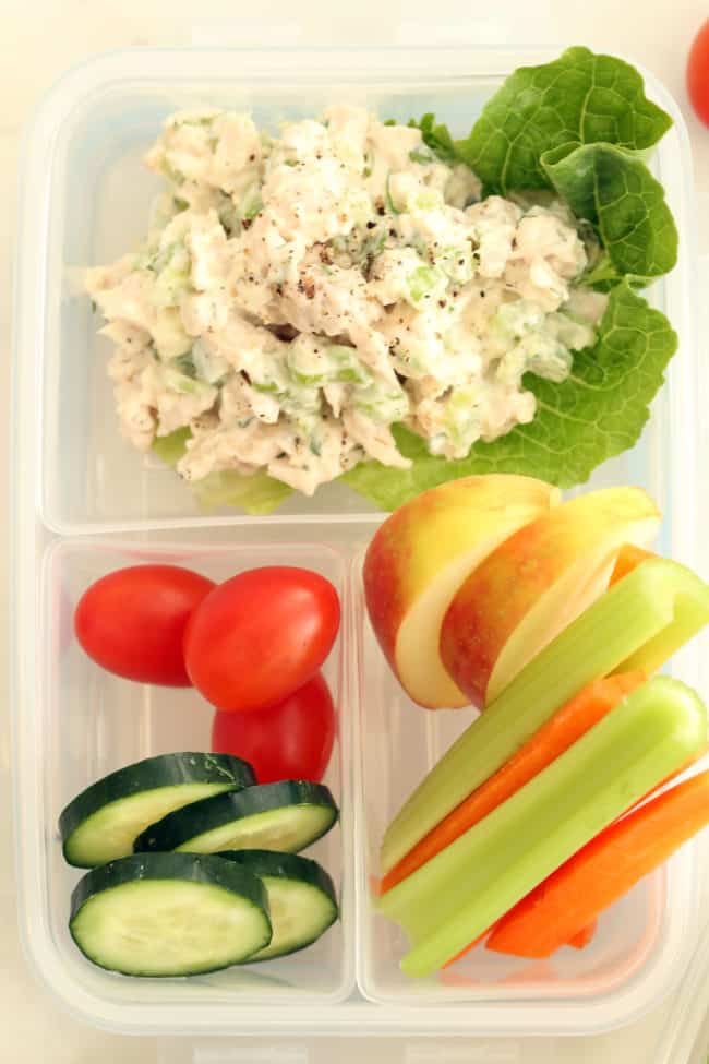 A clear plastic lunch box filled with tarragon chicken salad, cherry tomatoes, cucumber and celery and carrot sticks.