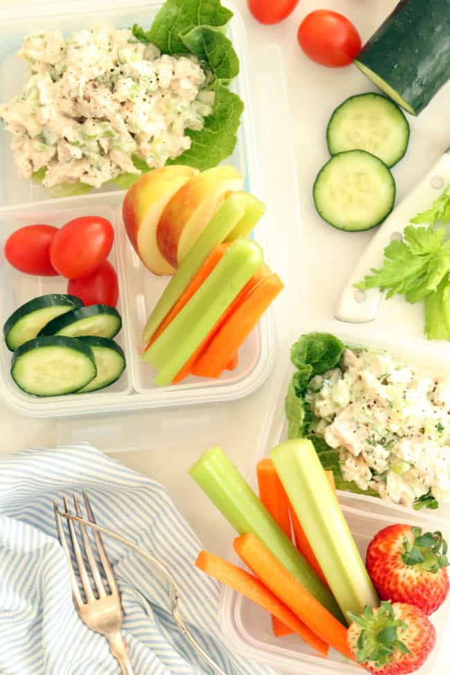 A plastic lunch container with tarragon chicken salad and celery and carrot sticks.