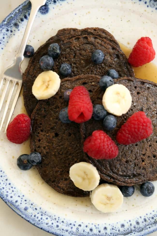 A blue and white plate filled with flapjacks drizzled with syrup and topped with fruit.