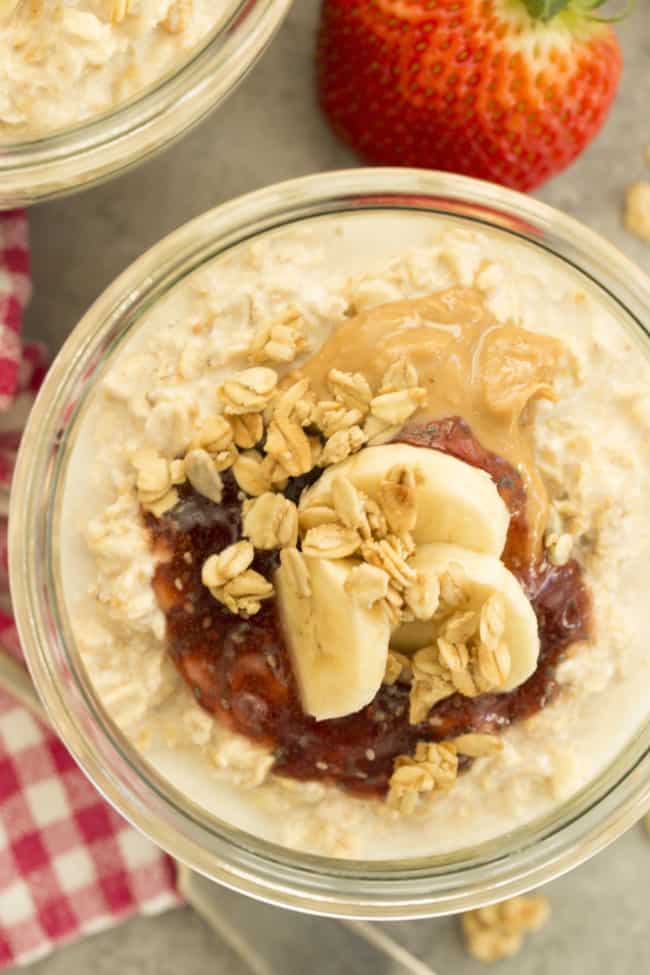 Clear glass bowl filled with overnight oats, peanut butter, jelly and slices of banana.