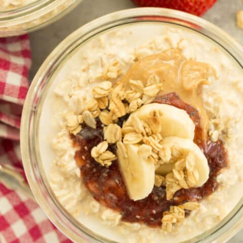 A glass bowl filled with oatmeal, peanut butter, jelly and banana slices.