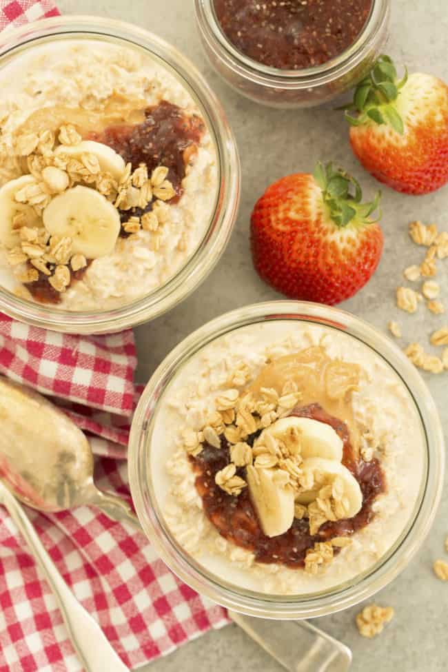 Two glass bowls filled with oatmeal, peanut butter, jelly and banana slices.