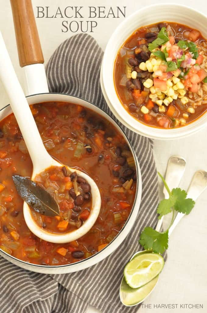 A white pot filled with Black Bean Soup. A ladle rests in the pot and a white bowl filled with the soup sits next to the pot.