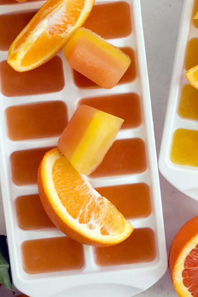 A white ice cube tray filled with citrus cubes (made with orange juice and grapefruit juice).