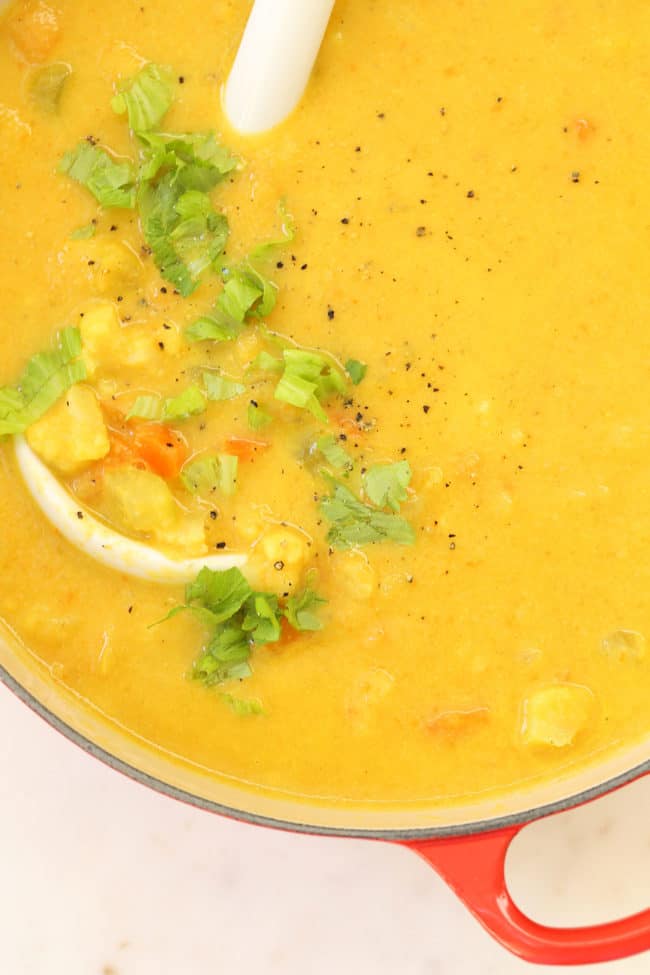 A red pot filled with cauliflower chowder soup. A white ladle rests in the bowl.