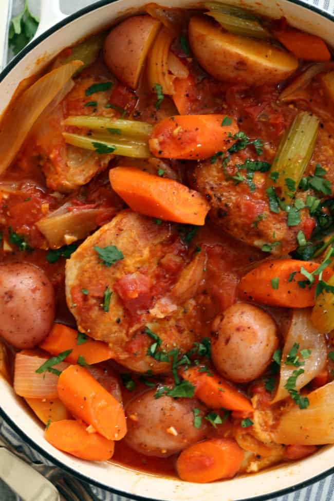 A white Dutch oven filled with cooked poultry and vegetables for stew.