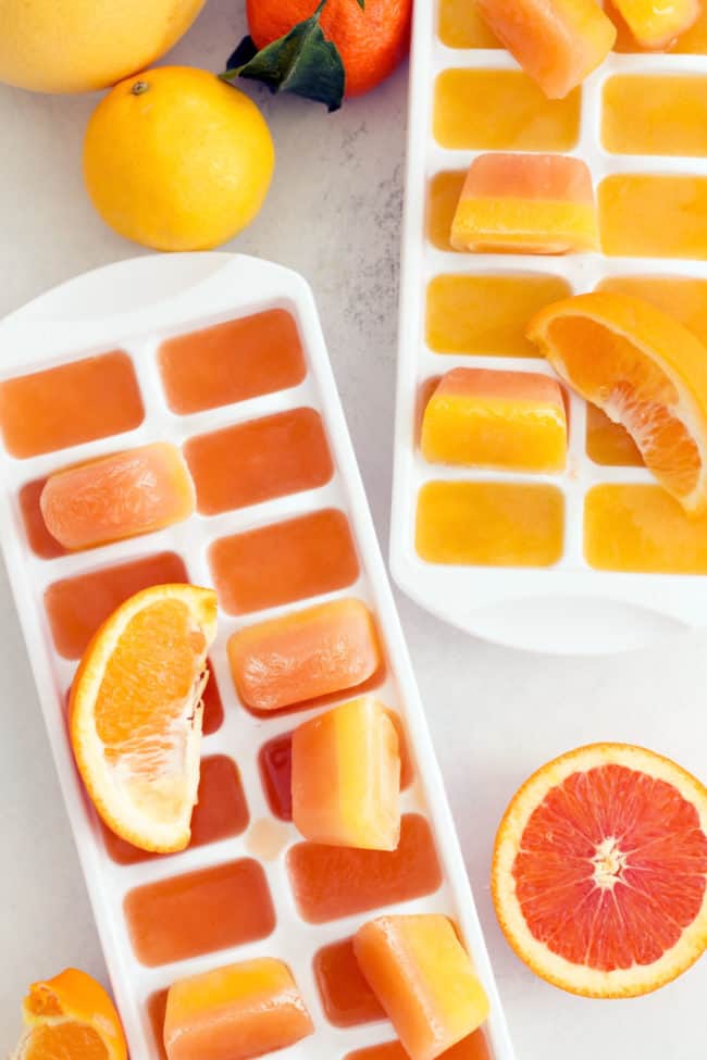 Two white ice cube trays filled with citrus ice cubes.