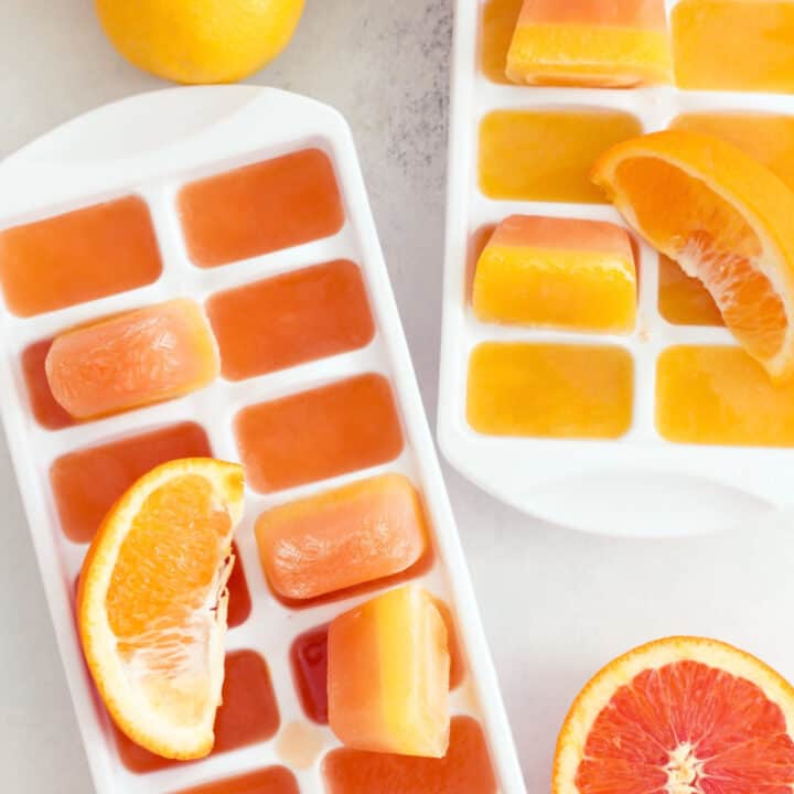 Two white ice cube trays filled with frozen orange juice ice cubes.