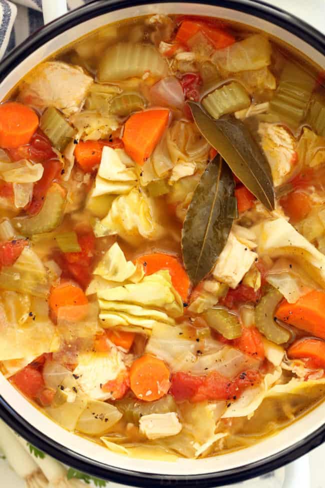 A white pot filled with carrots, celery and chicken.