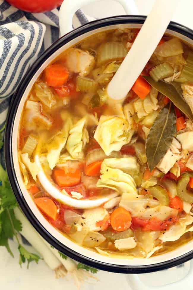 A white pot filled with chicken vegetable soup.