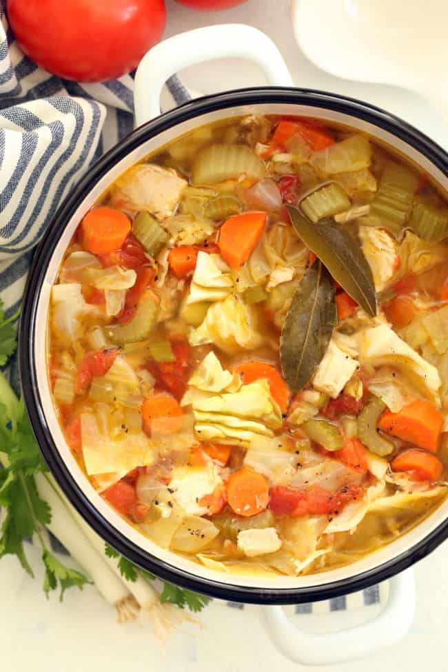 A white pot filled with chicken soup with vegetables.