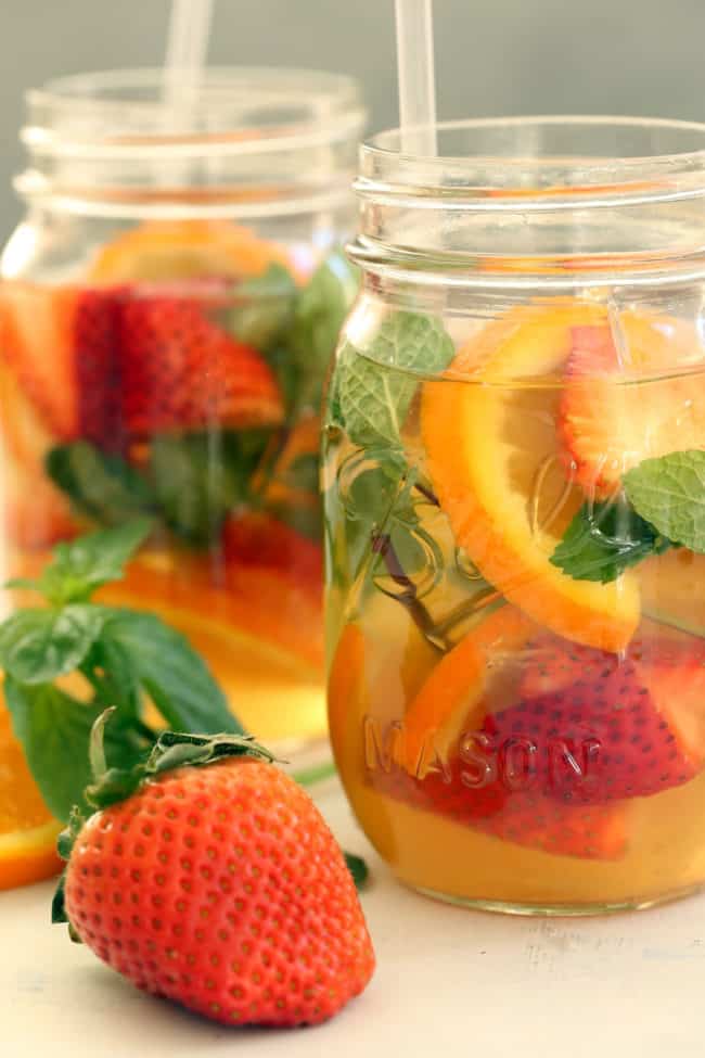 Two mason jars of turmeric tea with fruit and mint.