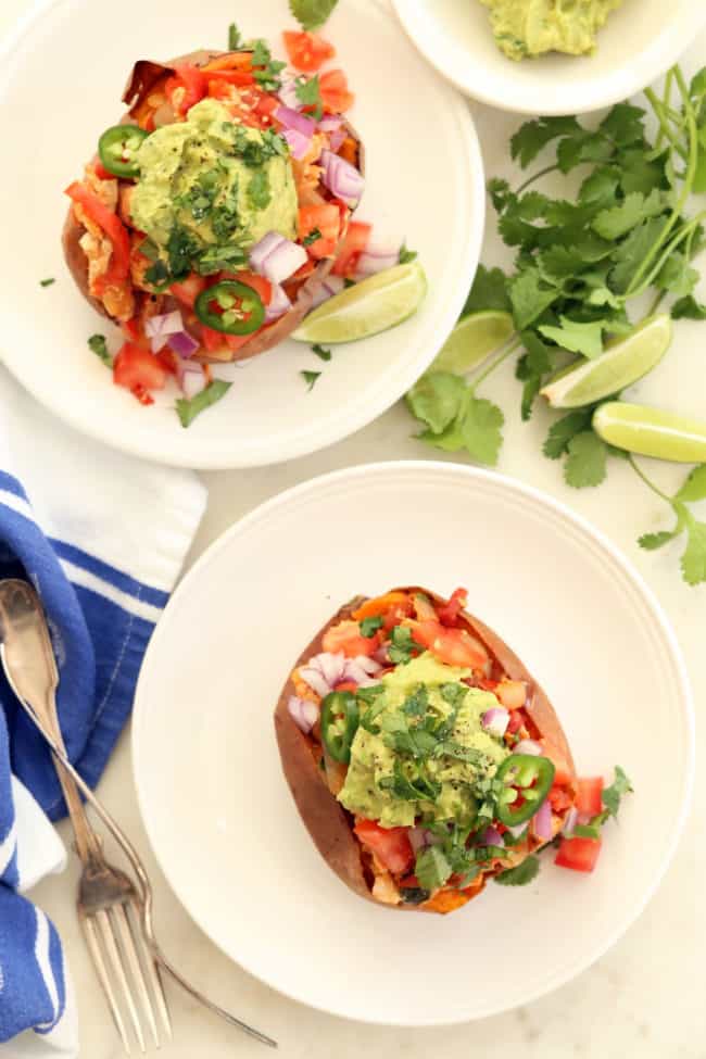 Two white plates with Mexican chicken stuffed sweet potatoes on them.