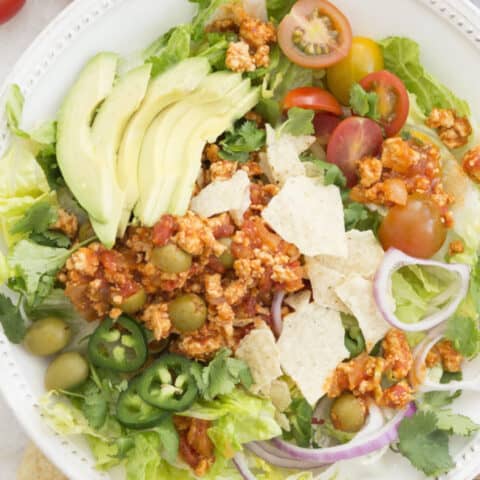 White bowl with tossed salad topped with Cuban picadillo recipe.