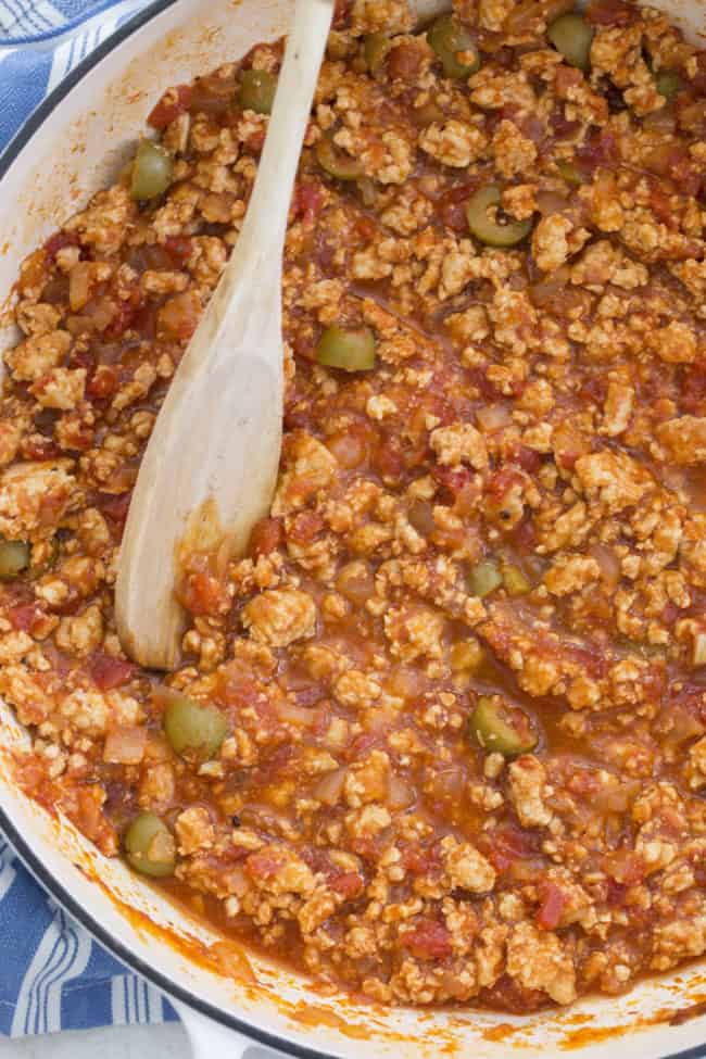 white Dutch oven filled with Cuban picadillo. A wooden spoon rests on the Dutch oven.