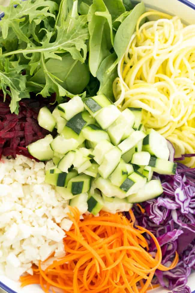 A white bowl of grated raw beets, sliced cabbage, chopped kale and grated carrots 