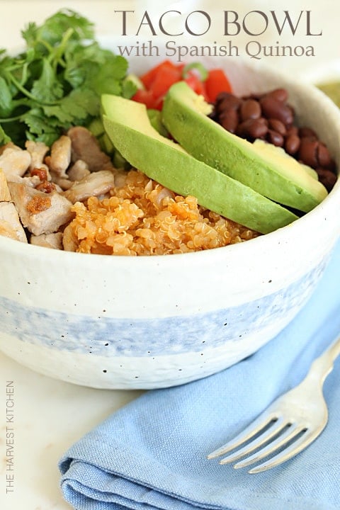 A white bowl of filled with grilled chicken, quinoa, black beans and avocado slices