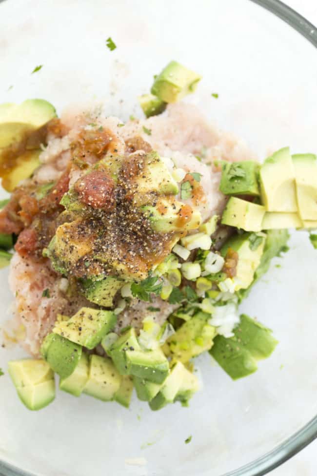 A clear mixing bowl filled with ground meet and chopped avocado.