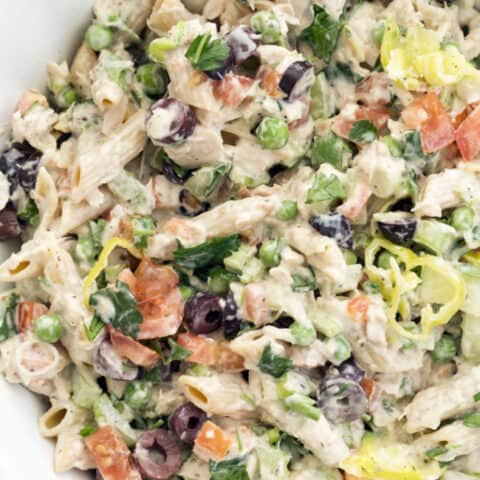 A white bowl filled with penne noodles, canned tuna, and vegetables tossed in a dressing.