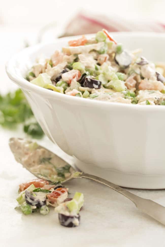 A white bowl filled with tuna pasta salad. A silver serving spoon sits next to the bowl.