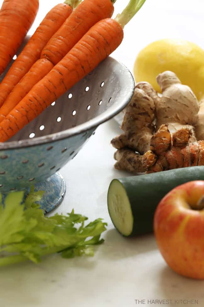 A blue colander filled with celery, cucumber, ginger root and apple.