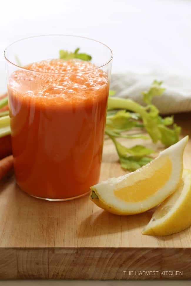 A clear glass of mixed vegetable juice with slices of lemons sitting next to it