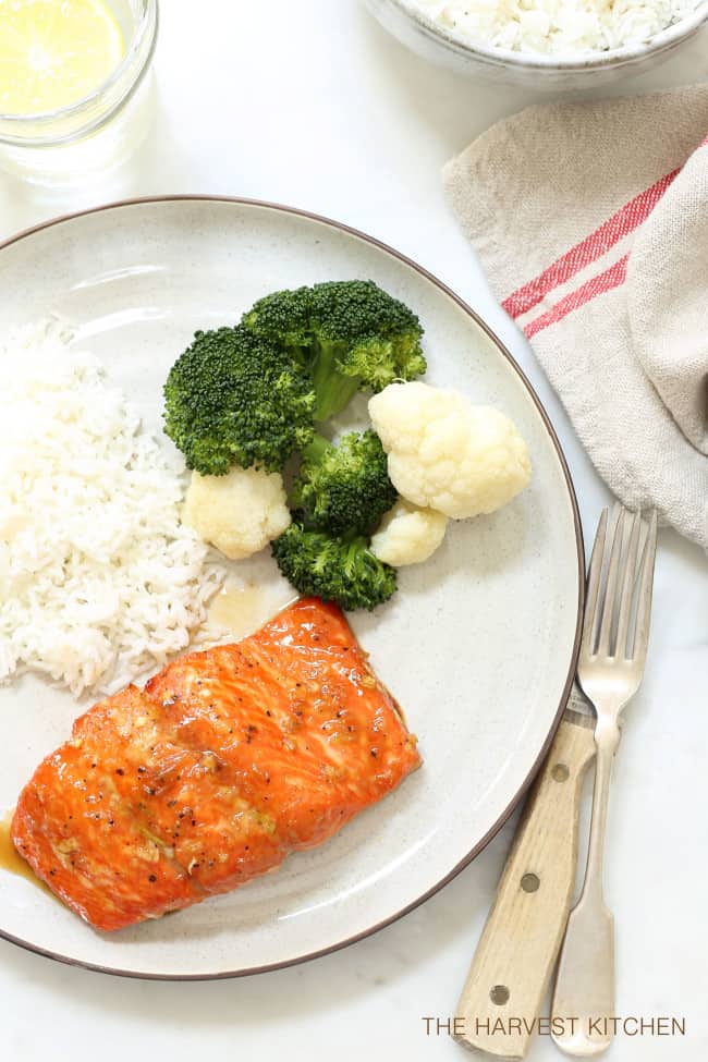 A white plate with rice, cooked broccoli and Orange Teriyaki Glazed Salmon.
