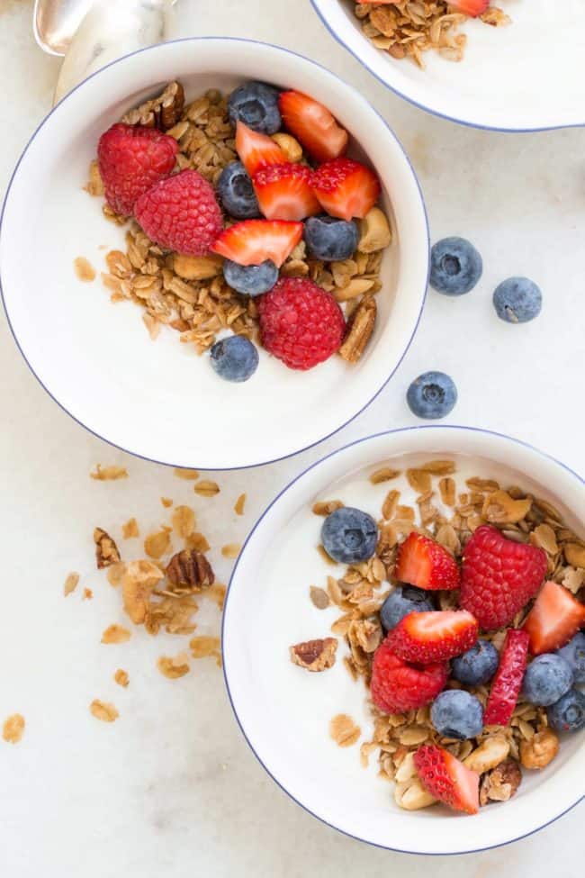 Two white bowls filled with yogurt, nuts and mixed berries