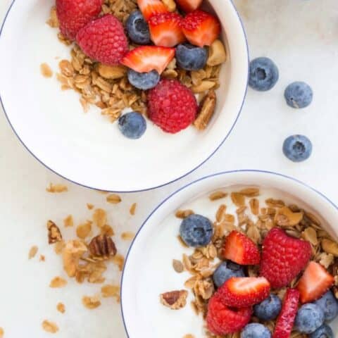 Two white bowls filled with yogurt, granola and mixed berries.