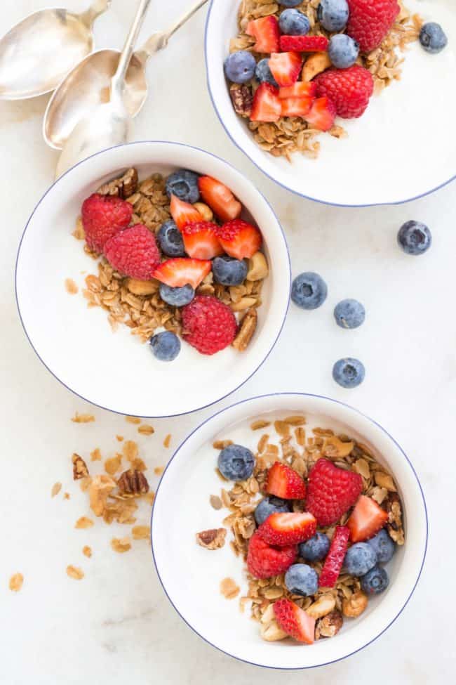 Three white bowls filled with yogurt, healthy granola and mixed berries.