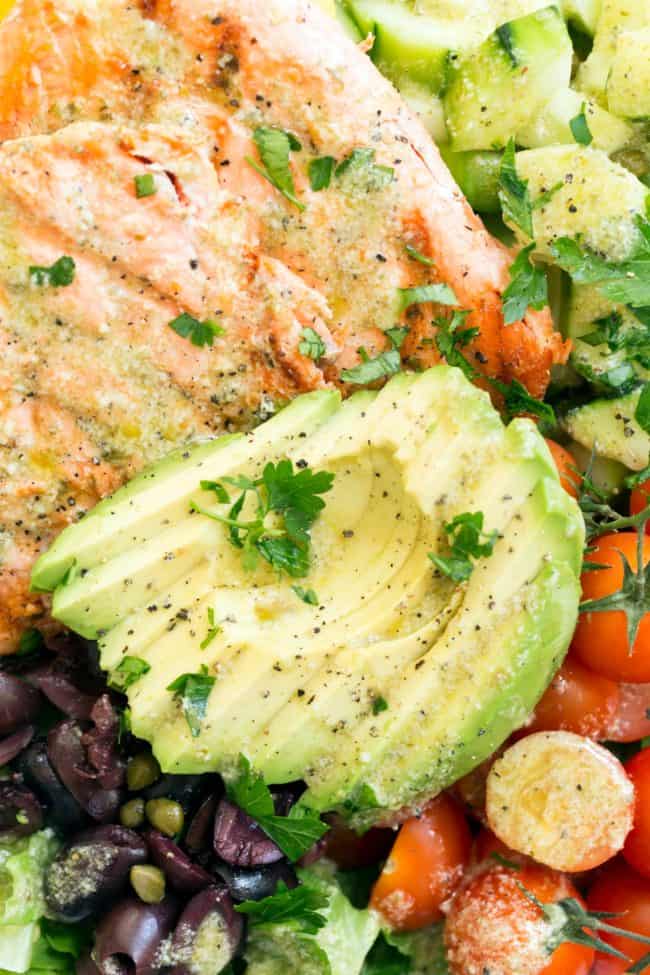 bowl filled with lettuce, cooked fish filets, slices of avocado, cherry tomatoes, cucumber and kalamata olives