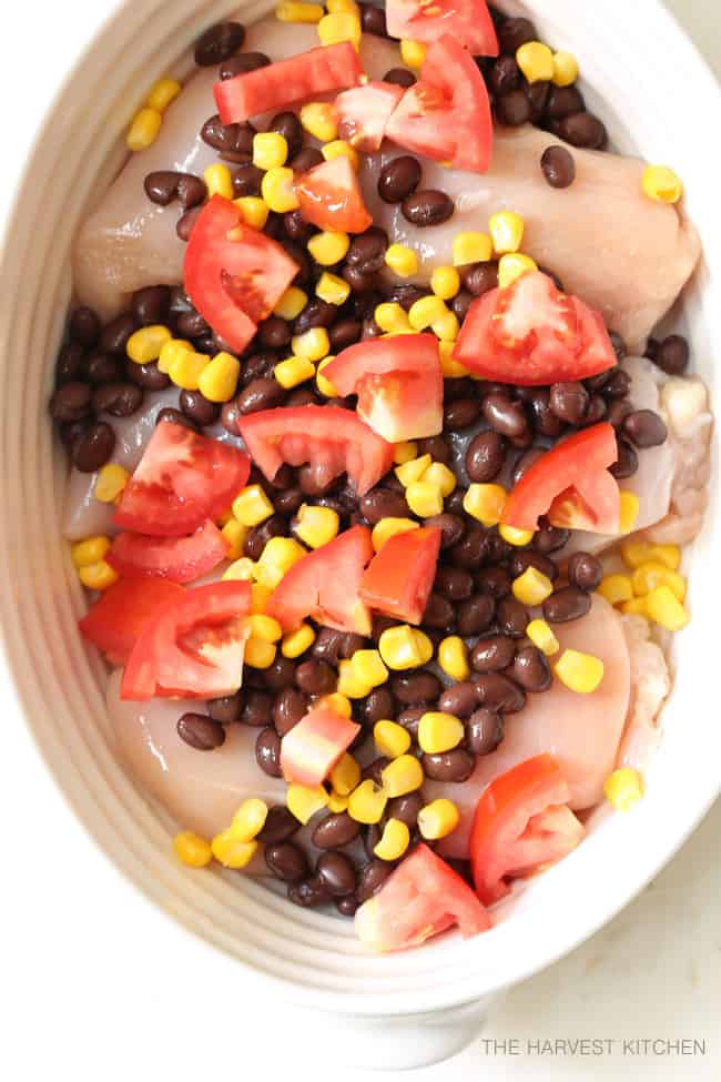 A white casserole dish filled with chicken, black beans, corn and chopped tomatoes.