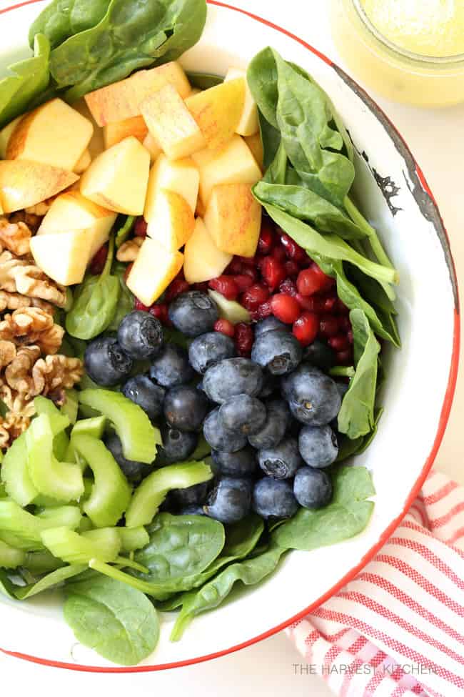A white bowl of mixed mixed vegetables, fruits and walnuts. 