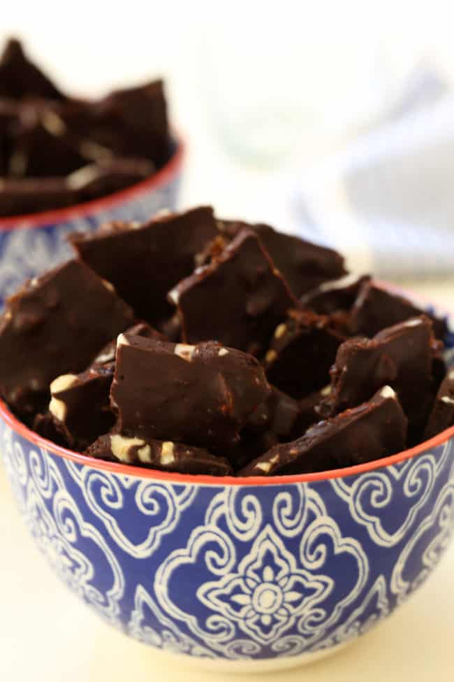 A blue and white bowl filled with pieces of dark chocolate almond bark.