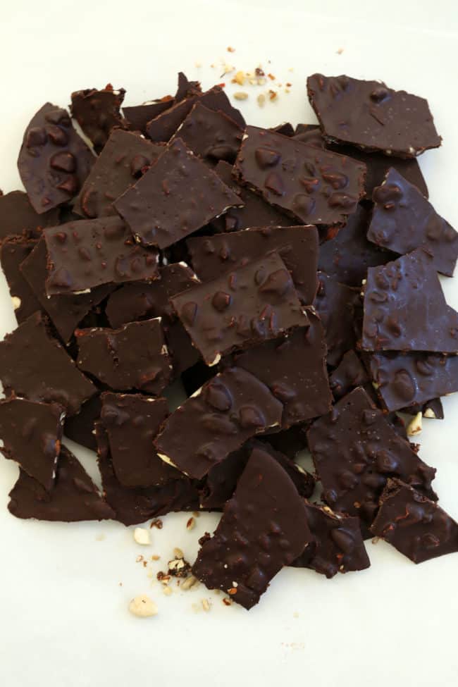 Dozens of large pieces of dark chocolate almond bark scattered on white counter.