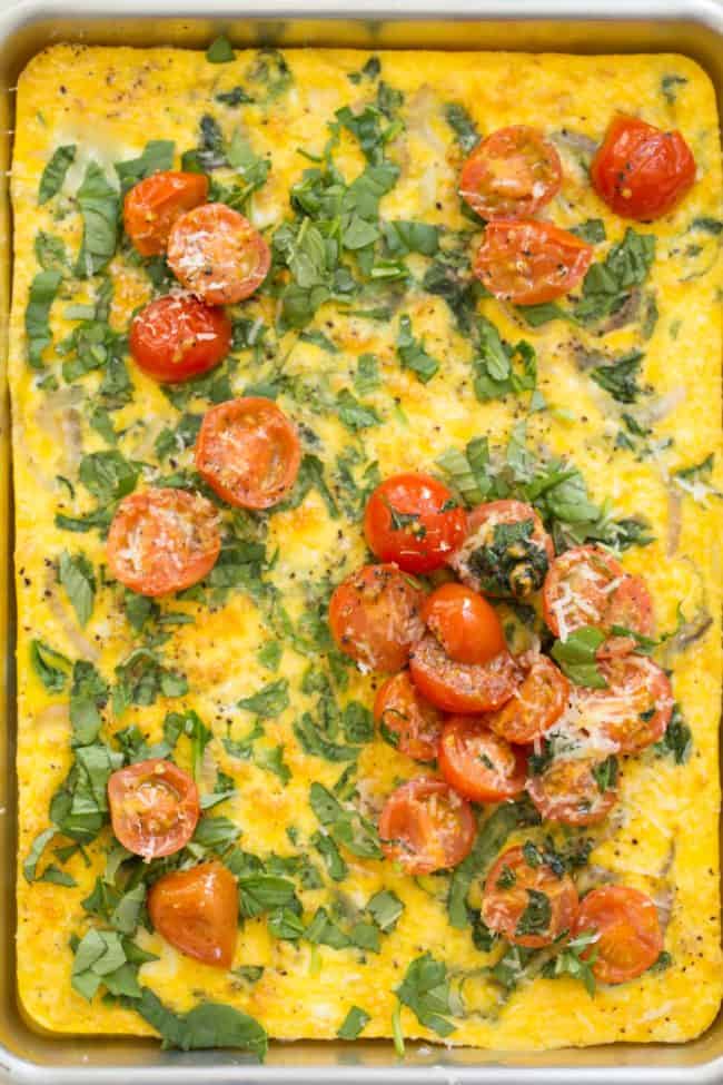 A cookie sheet with a baked spinach leek and onion frittata with pan roasted tomatoes on top.