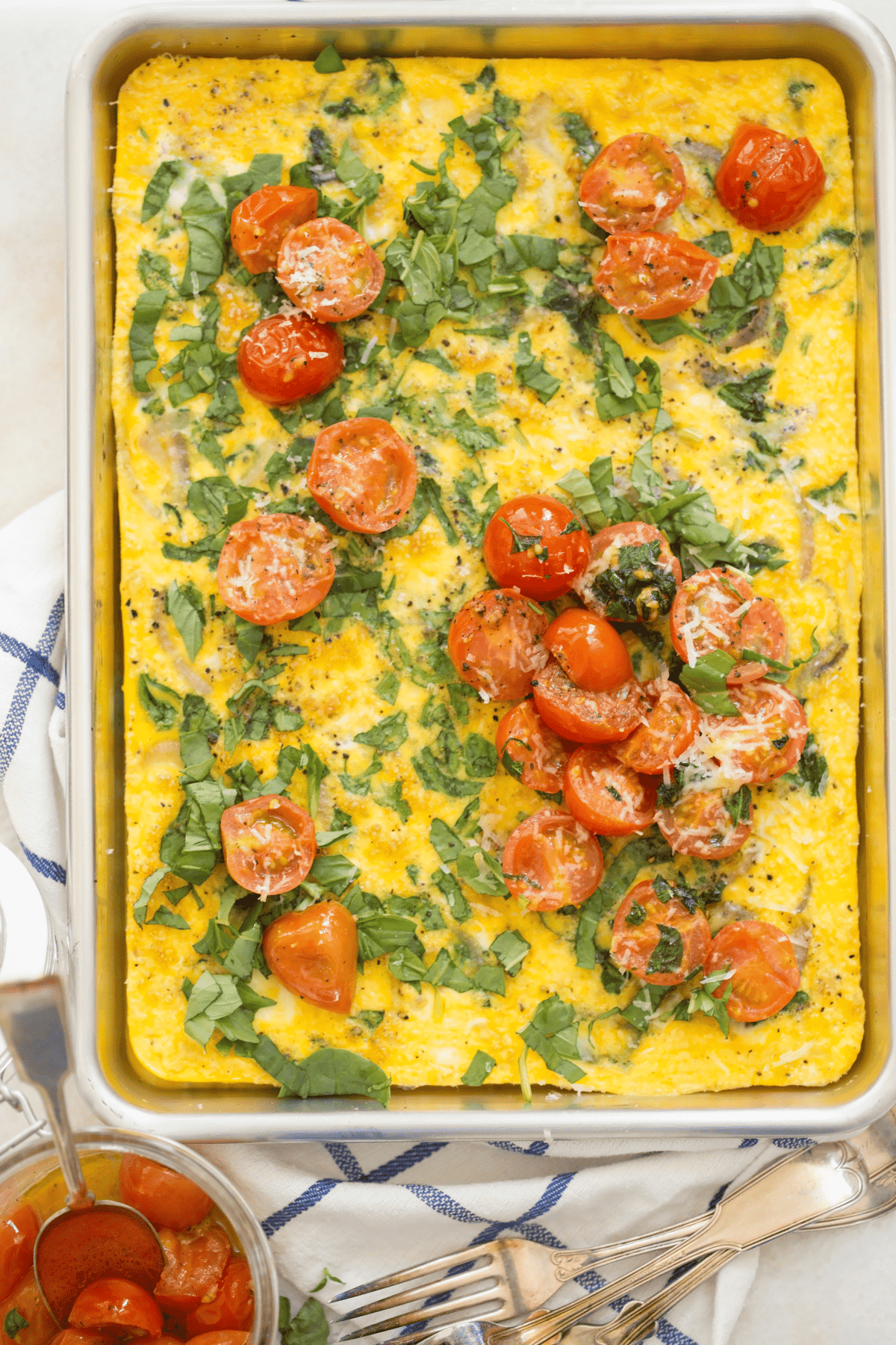 A cookie sheet filled with baked eggs with pan roasted tomatoes on top.