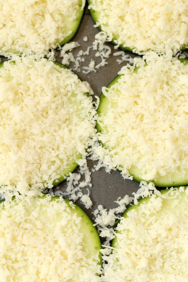 Sliced zucchini chips dusted with grated Parmesan cheese on a cookie sheet.