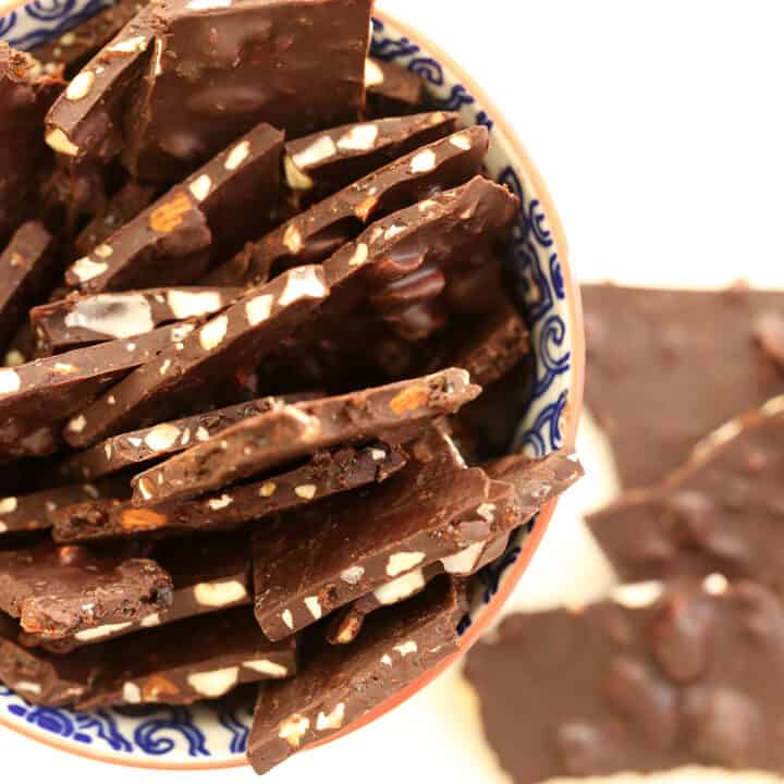 A blue and white bowl filled with large pieces of dark chocolate almond bark.