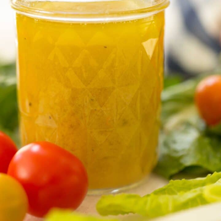 mason jar filled with citrus vinaigrette with lettuce and cherry tomatoes in the background
