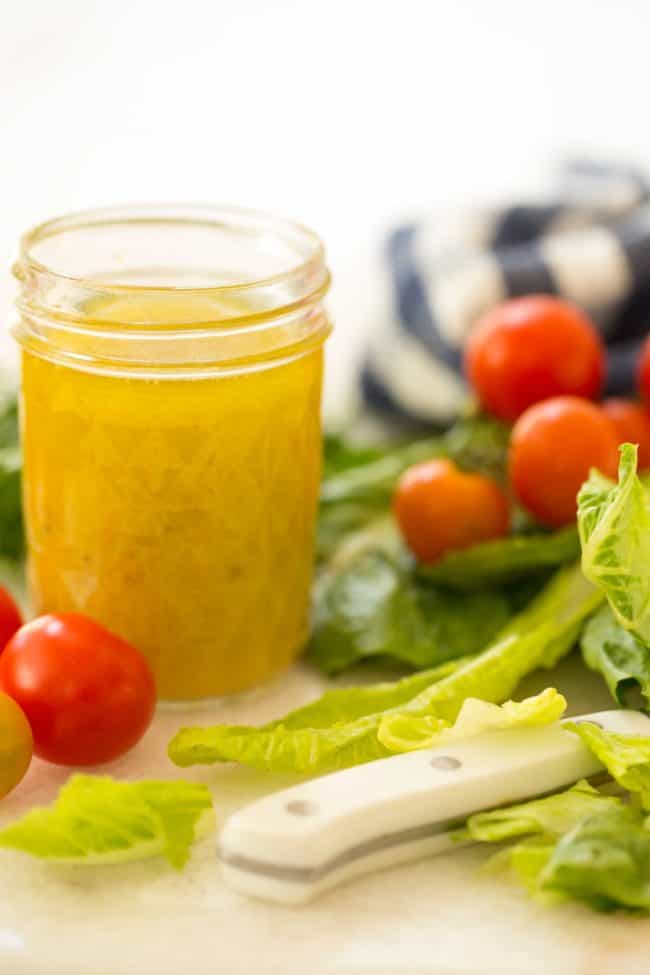 mason jar filled with citrus vinaigrette with lettuce and cherry tomatoes in the background with a blue and white striped kitchen towel