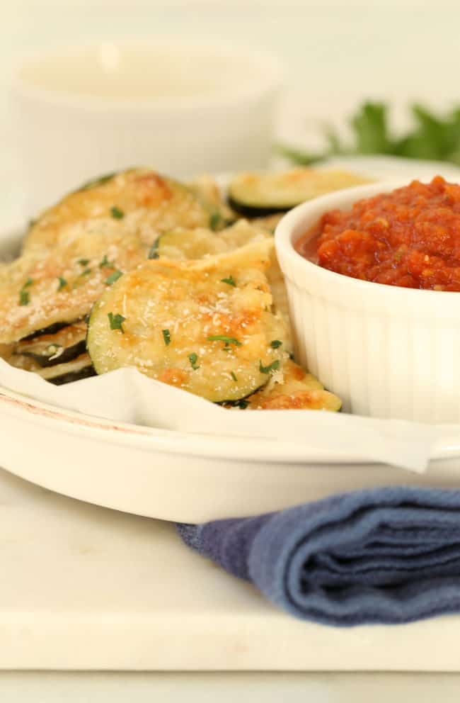 A white serving plate filled with oven baked zucchini chips. 