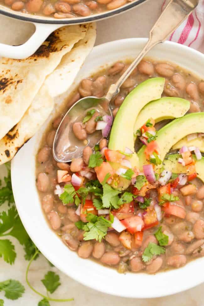 A white bowl filled with pinto beans and garnished with avocado.