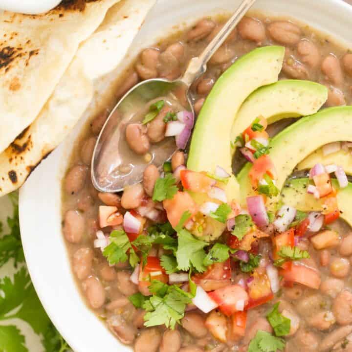 A white bowl filled with Mexican Pinto Beans garnished with avocado slices.