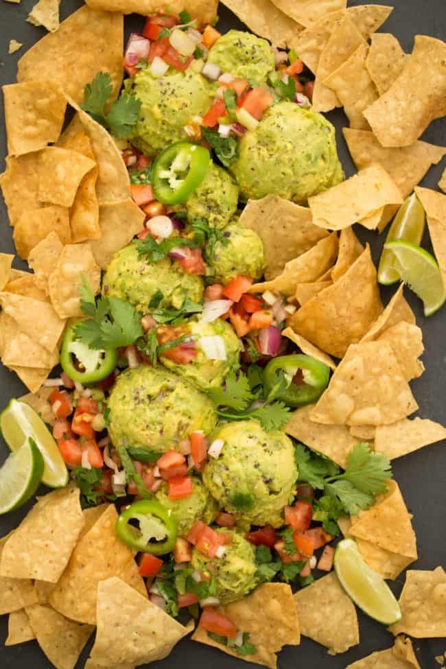 A platter with scoops of chunky guacamole and pico de gallo and tortilla chips.